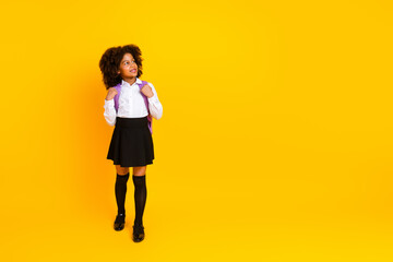 Adorable schoolgirl with backpack in uniform smiling against bright yellow background, showcasing...