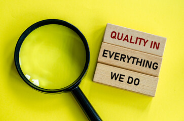 Top view of Quality In Everything We Do text on wooden blocks on yellow background with magnifying...