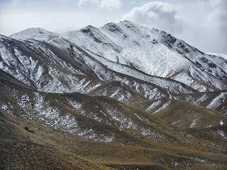 Scenic landscape of snow-covered mountains and dry grassy hills under an overcast sky. Captured...