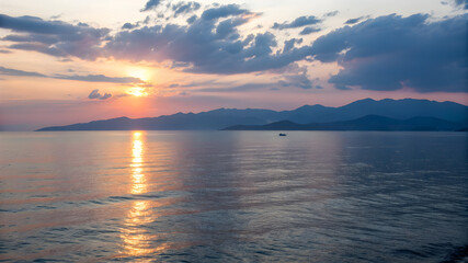 Obraz premium A vibrant sunset casts orange and pink hues over the sea, with majestic mountains silhouetted in the background