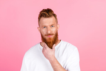 Handsome young man with a red beard poses thoughtfully in a casual white t-shirt against a pink...