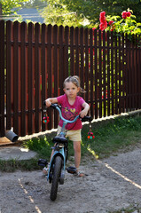 Young child standing by bicycle in a garden with flowers and fence during sunny afternoon