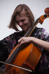 Woman playing cello, smiling, wearing floral robe.