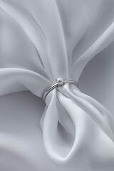 A simple yet elegant silver ring is positioned on softly draped white fabric. The smooth surface of...