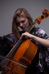 Woman playing cello, wearing floral robe, gray background.
