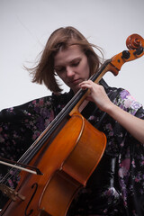 Woman playing cello, wearing floral kimono, against white background.