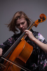 Woman playing cello, wearing floral kimono, gray background.