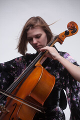 Woman playing cello, wearing floral kimono, against white background.