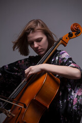 Woman playing cello, wearing floral robe, studio shot.