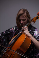 Woman playing cello, wearing floral kimono, studio shot.