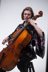 Woman playing cello, wearing floral kimono, on white background.