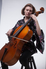 Woman playing cello, wearing floral kimono, studio shot.