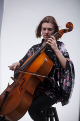 Woman playing cello, wearing floral robe, on white background.