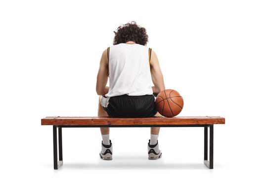 Rear view shot of a tired basketball player sitting on a bench with a ball