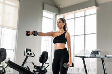 Fototapeta premium A woman is lifting weights in a gym. She is holding two dumbbells in each hand