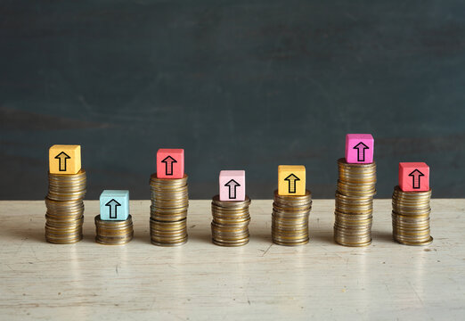 Business concept for financial growth, wealth mangement, making money or interest rate increase, inflation, high price, tax and tariffs rise . Arrow up sign on wooden cube blocks above stack of coins,