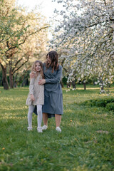 Obraz premium A mother and daughter are walking through a blooming apple orchard. they talk to each other. Concepts of family, mother and child, modern parenting.