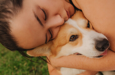 Close-up of a woman hugging a Welsh Corgi in the park in sunny weather. Concept of walking a dog,...