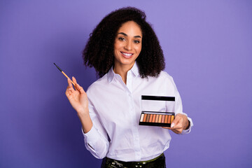 Confident Young Woman with Curly Hair Holding Makeup Products Demonstrating Beauty and Elegance...