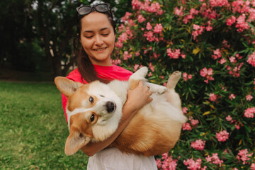 Close-up of a woman hugging a Welsh Corgi in the park in sunny weather. Concept of walking a dog,...