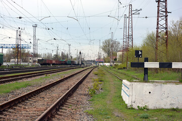 Railway track, metal lines of the railway with gray gears, green grass, large trees against the blue sky.