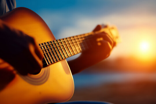 Musician strumming guitar as vibrant sunset casts warm glow. Outdoor setting with tranquil water in background enhances emotional moment. Concept of music, creativity, outdoor events