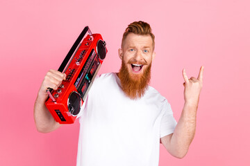 Excited bearded man holding retro boombox and gesturing with rock hand sign on vibrant pink background