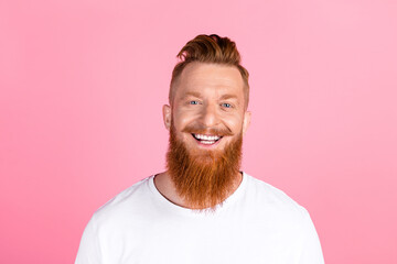 Cheerful man with stylish red beard and trendy hairstyle smiling against a pink background in a...