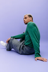 Stylish young Black man with dyed hair poses against a vibrant purple backdrop