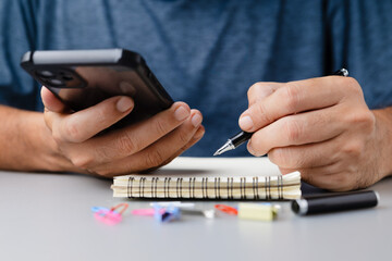 Man using smartphone while writing in notebook. A modern scene of multitasking, focus, and...