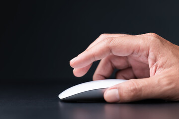 Close-up of a hand clicking a white wireless mouse on a dark background, representing digital work,...