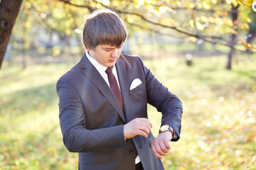 A man in a suit is checking his watch in a park