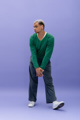 Naklejka premium Young man showcases stylish fashion against vibrant purple background in modern pose