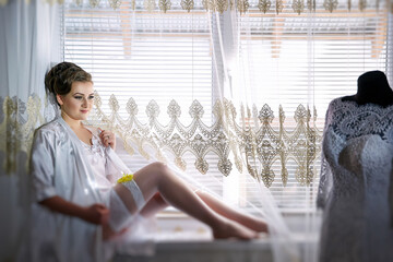 A woman in a white dress is sitting in front of a window with a lace curtain