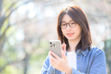 女性がスマホを両手で持ち微笑みながら見つめる春の光の中の柔らかい日常風景