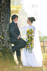A bride and groom are posing for a picture in front of a tree