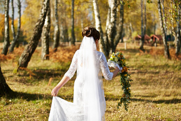 A bride is walking through a field with a bouquet of flowers