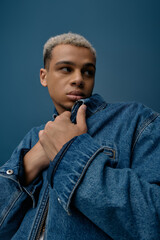 Young man in stylish denim jacket poses confidently against a blue background