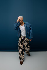 Stylish young man with dyed hair and denim jacket striking a pose against blue backdrop