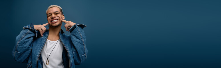 Young man with dyed hair shows style in denim jacket against blue backdrop