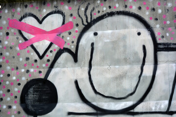 Graffiti, drawn with a white, black, pink spray drawing of a man in the form of a smiley, which hugs a hare with a crossed-out heart.