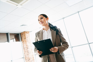 Confident businesswoman holding a clipboard in a modern office environment, showcasing professionalism and career ambition