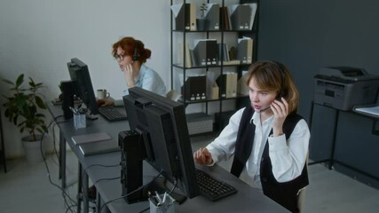 Two Caucasian young female call centre workers dressed formally consulting customers while working at office desks