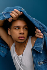 Young African American man models a denim jacket on a blue background