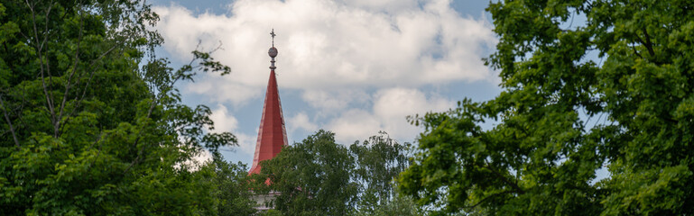 Tip of a red-roofed Christian church behind treetops — wide-angle view. 