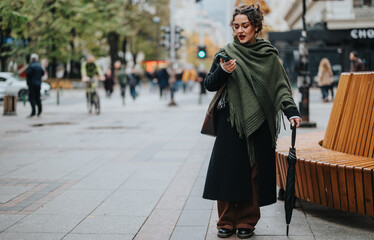 A woman in urban attire stands on a city street holding an umbrella and a phone. The background...