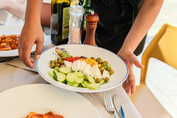 Waiters hands placing a salad on the table, close up, outdoor terrace in Italy.
