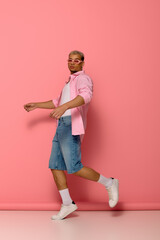 Young man with dyed hair and sunglasses poses confidently against a pink backdrop