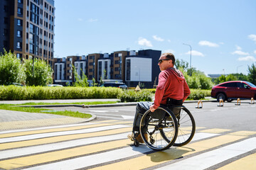 A middle -aged European in a wheelchair independently crosses the street at a pedestrian crossing
