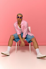 Stylish young man with dyed hair poses confidently against a vibrant pink backdrop